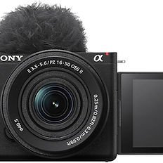 Front view of a Sony Alpha digital camera with a lens and flip-out screen, featuring a large microphone windscreen on top.